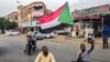 A Sudanese man sits with another in a street while waving a national flag during a mass demonstration against the country's ruling generals in the capital Khartoum, June 30, 2019. 