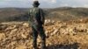 FILE - A Hezbollah fighter looks toward Syria while standing in the fields of the Lebanese border village of Brital, May 9, 2015. 