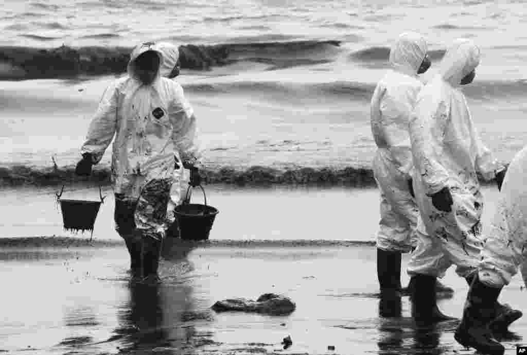 Para pekerja memindahkan minyak mentah dalam operasi pembersihan di Pulau Samet, Thailand (30/7).