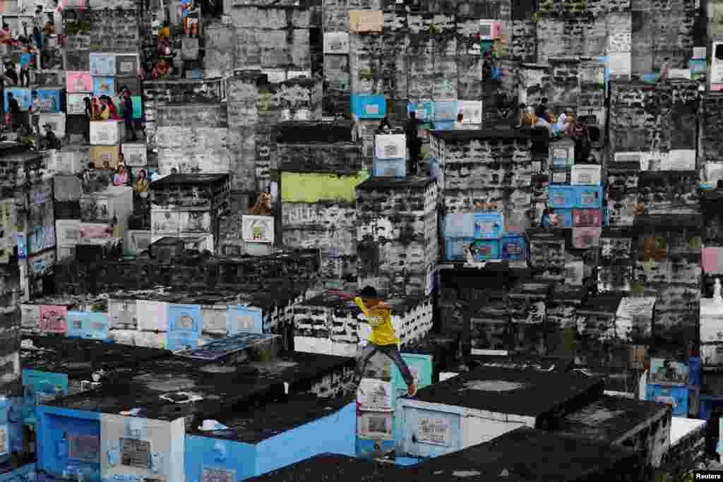 A boy leaps across apartment-style tombs as Filipinos visit the graves of their deceased loved ones to commemorate All Saints Day, at Barangka public cemetery in Marikina city, Metro Manila.