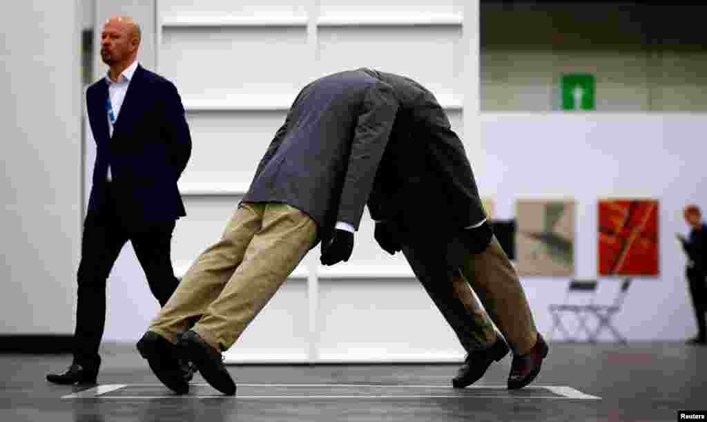 បុរស​ម្នាក់​ដើរ​កាត់​ស្នាដៃ​សិល្បៈ &laquo;Infinity Head&raquo; ដោយ​សិល្បករ​អាមេរិក​លោក Mark Jenkins ក្នុង​ពិព័រណ៍​ស្នាដៃ​សិល្បៈ​ Cologne Fine Arts Fair ក្នុង​ក្រុង Cologne ប្រទេស​អាល្លឺម៉ង់។