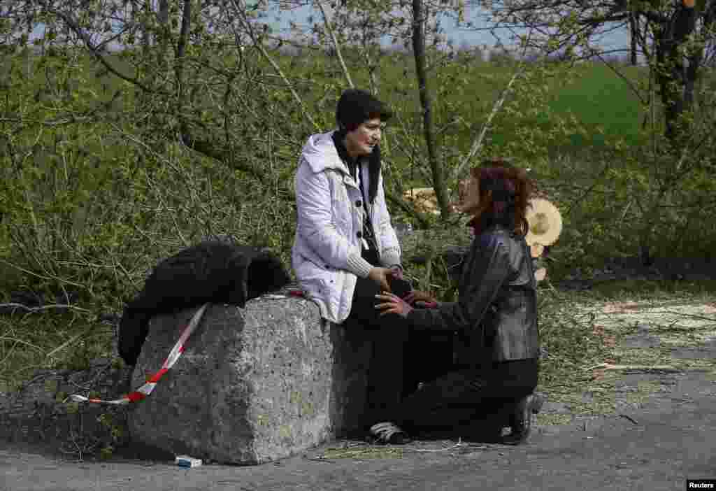 Istri seorang korban (kiri) duduk dekat pos pemeriksaan yang menjadi lokasi adu tembak dekat kota Slaviansk, Ukraina (20/4). (Reuters/Gleb Garanich)
