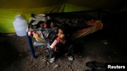 A Pakistani Christian girl drinks milk as her brother sleeps, in a tent provided for Christian families whose homes were set on fire by a mob, in Badami Bagh, Lahore, Pakistan, March 13, 2013.