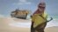 FILE - A masked Somali pirate stands near a Taiwanese fishing vessel that washed up on shore after the pirates were paid a ransom and released the crew, Sept. 23, 2012.