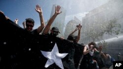 Anti-government demonstrators brace against the force of a police water canon during a general strike in Santiago, Chile, Oct. 23, 2019. 