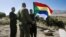 FILE - A member of the Druze community holds a Druze flag as he speaks to an Israeli soldier near the border fence between Syria and the Israeli-occupied Golan Heights, near Majdal Shams, June 18, 2015.