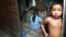 The child of a Cambodian prostitute stands in the doorway of a Phnom Penh slum shack as a group of sex workers play cards to pass the time, in this July 10, 2002 file photo.