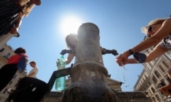 A tourist refreshes himself and fills bottle of water in a "Nasone" fountain in the center of Rome on Aug. 12, 2020.
