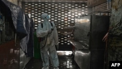 A worker wearing personal protective equipment (PPE) sprays disinfectant in the Orussey market after it was temporarily closed following a few vendors testing positive for the Covid-19 coronavirus, Phnom Penh, Cambodia, April 4, 2021. (Photo by TANG CHHIN Sothy / AFP)