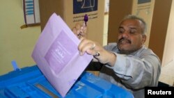 Seorang peserta pemilu memamerkan jarinya yang telah dicelup tinta sambil memasukkan surat suaranya ke dalam kotak di salah satu TPS di Baghdad (20/4).