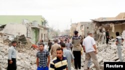 Warga berdiri di antara reruntuhan bangunan yang hancur akibat ledakan dua bom mobil di Tuz Khormato, Irak utara (21/5).