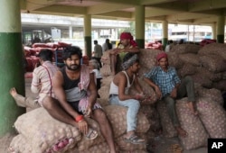 FILE - Workers rest on bags of onions at a wholesale market in Hyderabad, India, Friday, Aug. 5, 2022. (AP Photo/Mahesh Kumar A.)