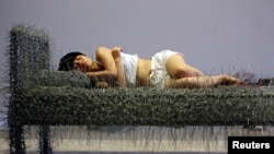 北京的周洁在行为艺术个展中躺在钢丝床上，有时裸睡