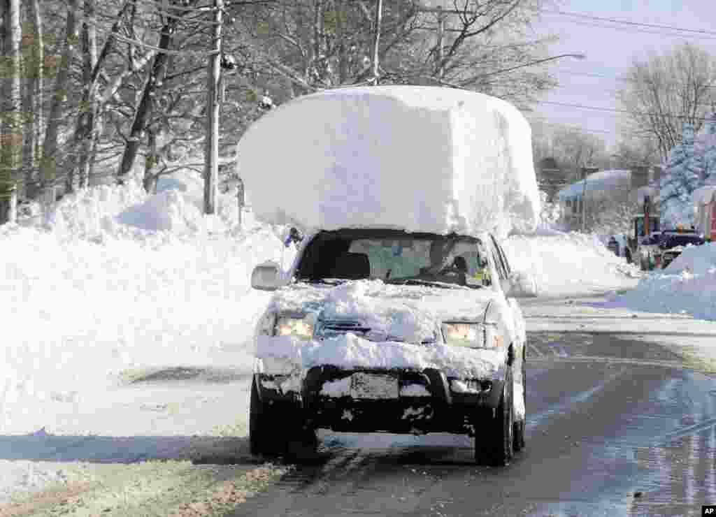 A vehicle, with a large chunk of snow on its top, drives along Route 20 after digging out after a massive snow fall in Lancaster, N.Y. Nov. 19, 2014.