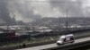 A firefighter watches smoke rising from a highway next to an ambulance, near the site of the explosions at the Binhai new district, Tianjin, August 13, 2015.