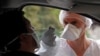 FILE - A medical worker administers a nasal swab to a patient at a drive-through coronavirus testing site near a hospital in Laval, France, July 15, 2020.
