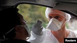 FILE - A medical worker administers a nasal swab to a patient at a drive-through coronavirus testing site near a hospital in Laval, France, July 15, 2020.