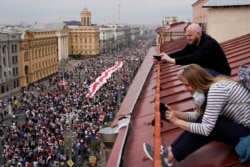 People take photos sitting on the roof as Belarusian opposition supporters with a huge old Belarusian national flag march to Independence Square in Minsk, Belarus, Aug. 23, 2020.