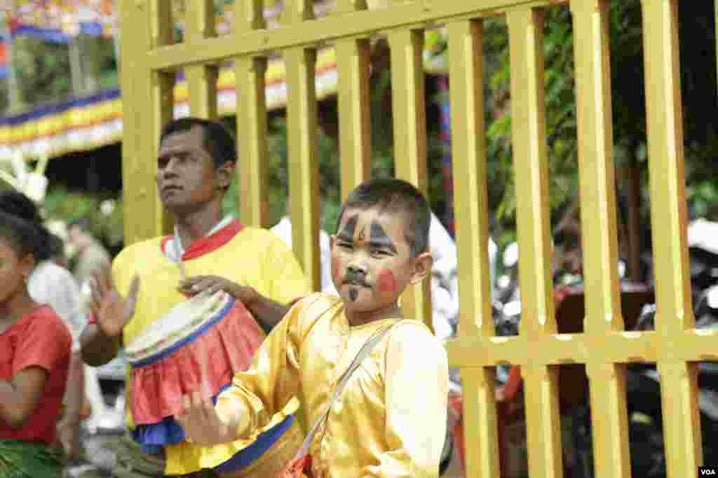 កុមារា​​ម្នាក់​កំពុង​វាយស្គរ​​នៅ​ខាង​មុខ​ក្លោង​ទ្វារ​មាត់​ដើម្បី​ស្វាគមន៍​ពុទ្ធ​បរិស័ទ​ដែល​អញ្ជើញ​មក​វត្ត​មួយ​កណ្តាល​រាជធានី​ភ្នំពេញ​កាលពី​ព្រឹក​ថ្ងៃសៅរ៍​ ទី​១៦ ខែ កញ្ញា​​ ឆ្នាំ២០១៧។​(ទុំ ម្លិះ/VOA)