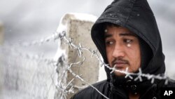 A migrant stands next to a fence during snowfall at the Lipa camp, outside Bihac, Bosnia. A fresh spate of very cold winter weather on has brought more misery for hundreds of migrants who have been stuck for days in a burnt-out camp.