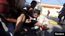 Para demonstran mengangkut temannya yang terluka akibat tembakan oleh para milisi di Tripoli hari Jumat (15/11). 