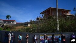 FILE - People stand in line outside the Maria Simmons elementary school waiting to be inoculated with the Moderna COVID-19 vaccine as part of a mass vaccination campaign, in Vieques, Puerto Rico, March 10, 2021.