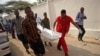 Quelques personnes portent le corps d'une victime de l'explosion de voiture près de l'hôtel Doorbin à Mogadiscio, le 24 février 2018. AFP PHOTO / Mohamed ABDIWAHAB