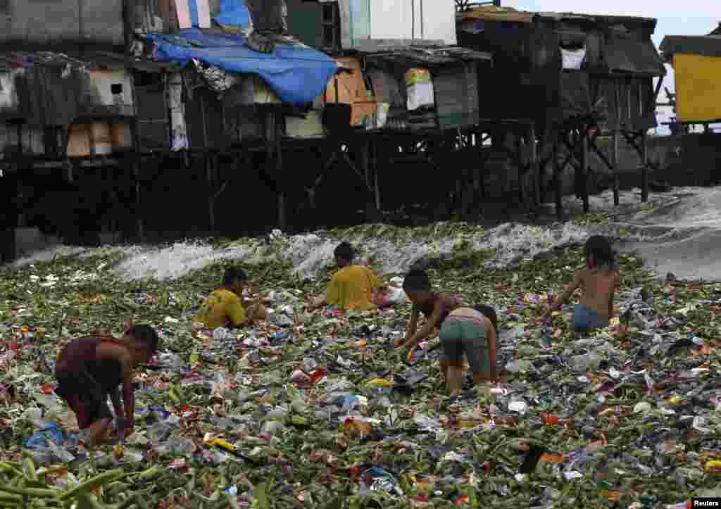 Anak-anak duduk sambil menyaring sampah daur ulang yang mengambang untuk dijual, di saat gelombang kuat melanda sepanjang pantai Teluk Manila, dekat daerah kumuh di Manila, Filipina.
