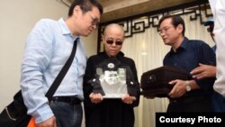 刘晓波遗孀刘霞手捧遗像。刘晓波弟弟刘晓瑄（右）和刘霞弟弟刘晖陪伴（沈阳市政府公布图片）