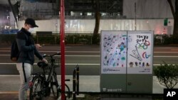 A man wearing a mask looks at his smartphone next to a poster celebrating the Tokyo 2020 Olympics Tuesday, March 3, 2020, in Tokyo. The Japanese government has indicated it sees the next couple of weeks as crucial to containing the spread of COVID…