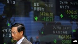 Seorang pria berjalan melewati papan yang menunjukkan nilai indeks Nikkei di Tokyo, Jepang.