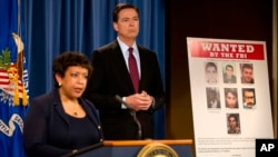 La ministre américaine de la Justice, Loretta Lynch, aux côtés du chef du FBI, James Comey, lors d'une conférence de presse à Washington, avec une affiche révélant le visage des sept Iraniens inculpés de piratage informatique et recherchés par le FBI, 24 mars 2016.