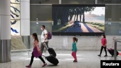 FILE - Travelers wearing protective face masks make their way through the arrivals section of the international terminal of Kingsford Smith International Airport the morning after Australia implemented an entry ban on non-citizens and non-residents.