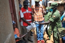 FILE - Member of Uganda's armed forces, and a Red Cross worker distribute foodstuffs to people affected by the lockdown measures aimed at curbing the spread of the new coronavirus, in the Bwaise suburb of Kampala, Uganda, April 4, 2020.