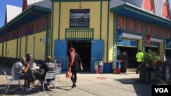 Customers sit outside the Caribbean Marketplace in Little Haiti, Miami, Florida. (Photo: S. Lemaire / VOA) 