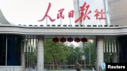 FILE - A man holding a smartphone walks past the headquarters of the Chinese Communist Party newspaper People's Daily, in Beijing, China, Oct. 6, 2018. 