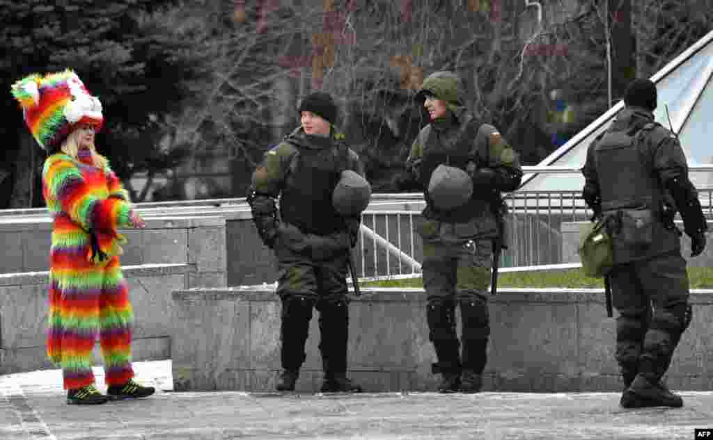 Tiga tentara Ukraina yang melakukan patroli di Lapangan Kemerdekaan di Kyiv, melewati seorang perempuan yang mengenakan kostum warna-warni.