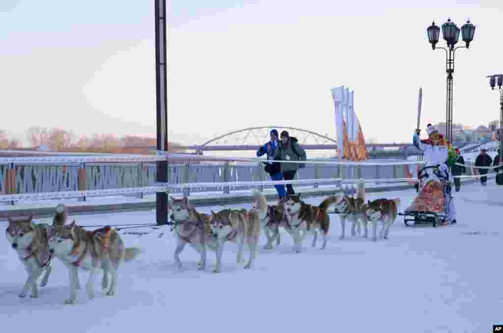 Pembawa obor olimpiade musim dingin Sochi, Mikhail Fateyev, membawa obor dengan naik kereta anjing di atas lapisan salju di pinggir sungai Tura, Tyumen, Siberia barat, Rusia. 