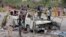 A Somali soldier, left, stands by the wreckage of a minibus that was destroyed in a suicide car bomb attack near the defense ministry compound in Mogadishu, Somalia, April 9, 2017.