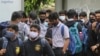 School students wearing face masks as a precaution against COVID-19 wait at a bus stop in Bengaluru, India, Nov. 30, 2021.