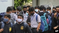 School students wearing face masks as a precaution against COVID-19 wait at a bus stop in Bengaluru, India, Nov. 30, 2021.