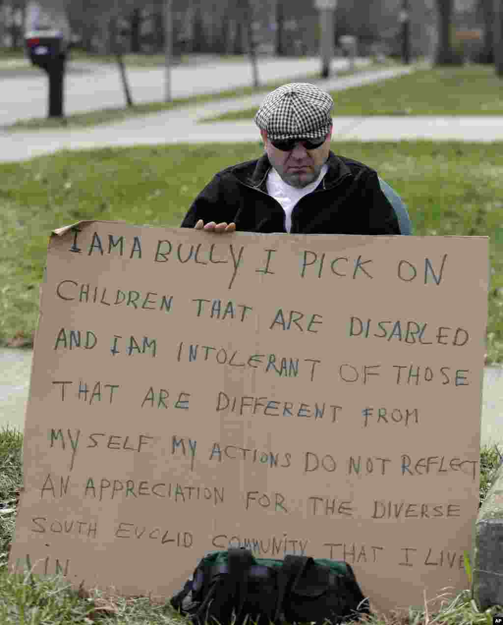 Edmond Aviv sits on a street corner holding a sign in South Euclid, Ohio declaring he's a bully, a requirement of his sentence because he was accused of harassing a neighbor and her disabled children for the past 15 years, April 13, 2014. 