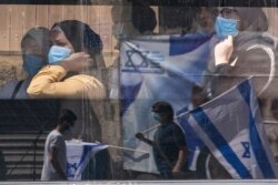 Women wearing face masks to protect from the coronavirus ride a public bus as they watch supporters of Prime Minister Benjamin Netanyahu wave flags outside the district court in Jerusalem, July 19, 2020.