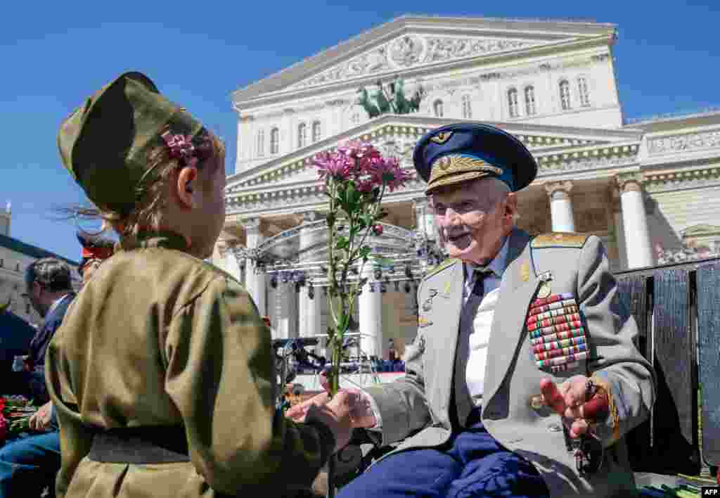 A child presents a flower to a World War II veteran in front of the Bolshoi Theater during Victory Day celebrations in downtown Moscow, Russia.