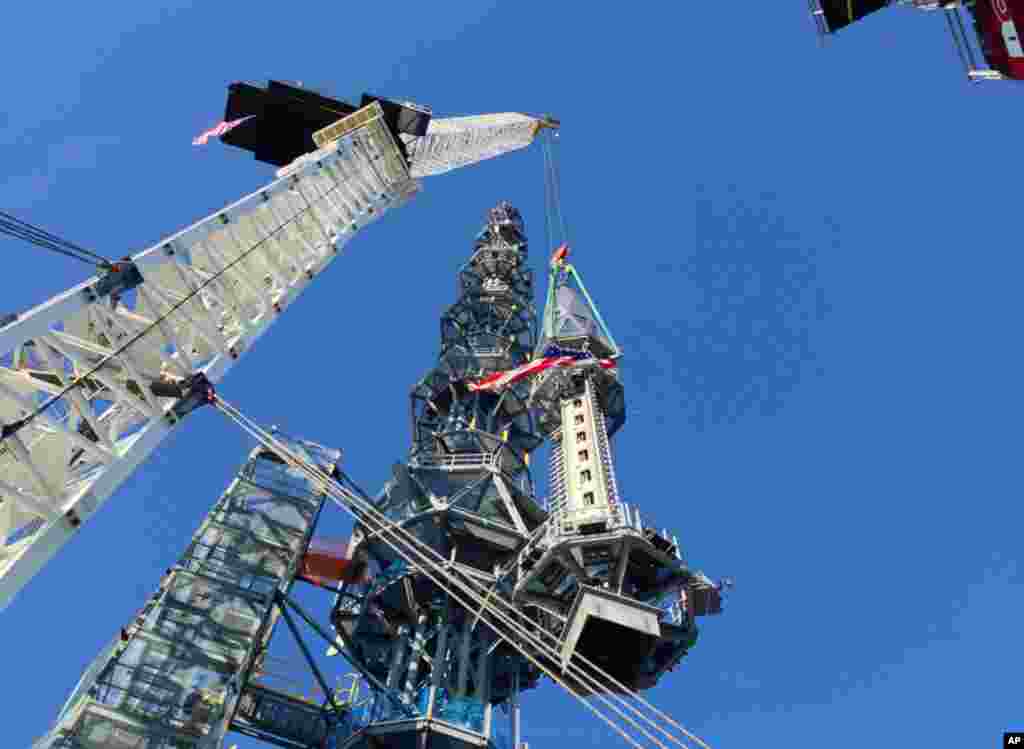 Puncak menara yang berwarna perak diangkat untuk dipasang di gedung One World Trade Center (10/5), membuat struktur bangunan menjadi setinggi 541 meter. Puncak seberat 758 ton itu akan menjadi antena penyiaran kelas dunia. (AP/Mark Lennihan)