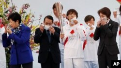 Tokyo Gov. Yuriko Koike, left, Tokyo 2020 Organizing Committee President Seiko Hashimoto, right, and attendees take off their face masks while preparing to pose for group photos during the Tokyo 2020 Olympic Torch Relay Grand Start.