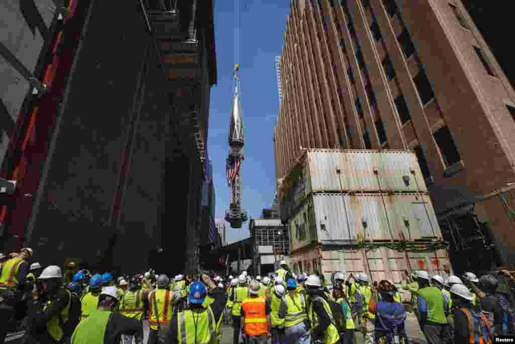 Para wartawan dan pekerja di Ground Zero mengambil foto saat bagian akhir puncak menara diangkat ke atas One World Trade Center, di New York.