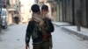 FILE - A Kurdish fighter from the People's Protection Units (YPG) carries his son as he walks along a street in Aleppo's Sheikh Maqsoud neighborhood, Feb. 18, 2014. Rebels with the Army of Islam and their allies said Tuesday they will continue fighting in the predominantly Kurdish neighborhood, despite a cease-fire.