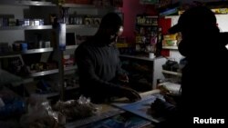 FILE - A shopkeeper counts change by the light of a battery-powered lamp during a load-shedding electricity blackout in Cape Town, South Africa, April 15, 2015.
