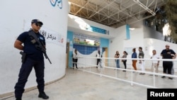 A police officer stands guard as people queue to cast their vote outside a polling station during a second round runoff of a presidential election in Tunis, Tunisia, Oct. 13, 2019. 